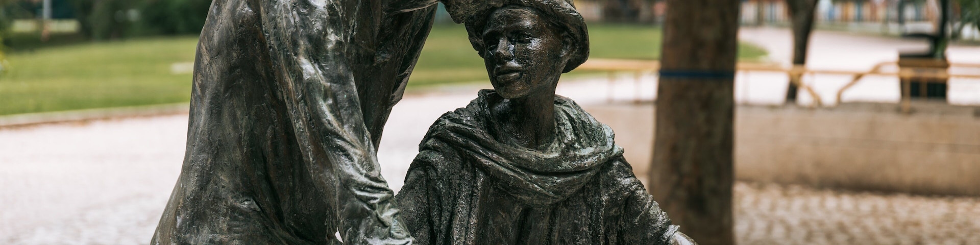 A statue of a person helping another on a bicycle in a park.