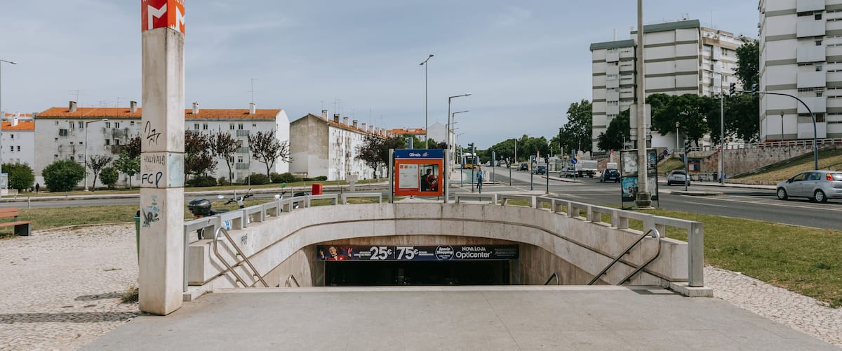 A metro station with a red and white sign, a bus stop, and a pedestrian bridge over a road.