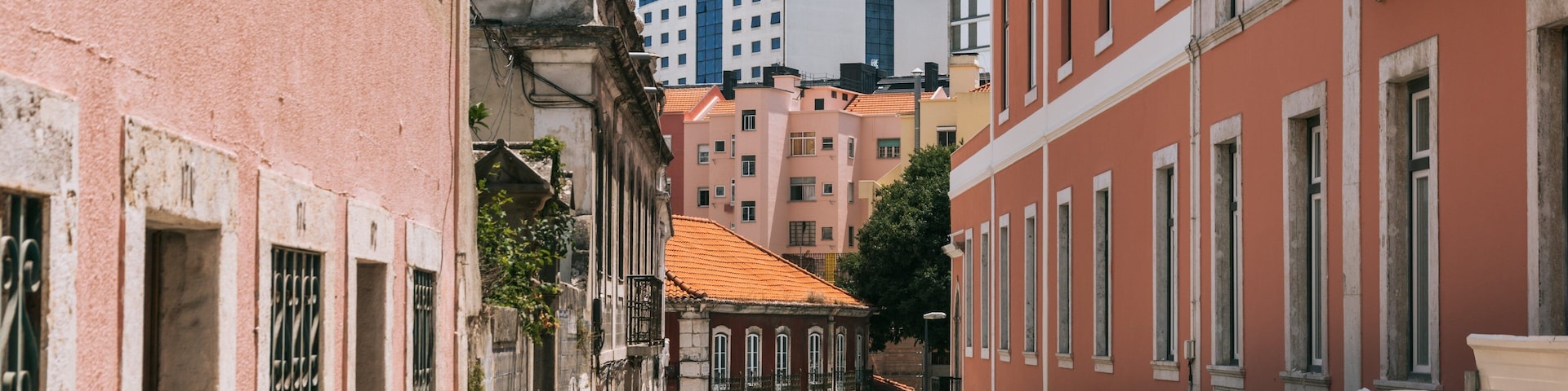 A narrow street lined with historic buildings, a modern blue skyscraper, and outdoor seating at a café.