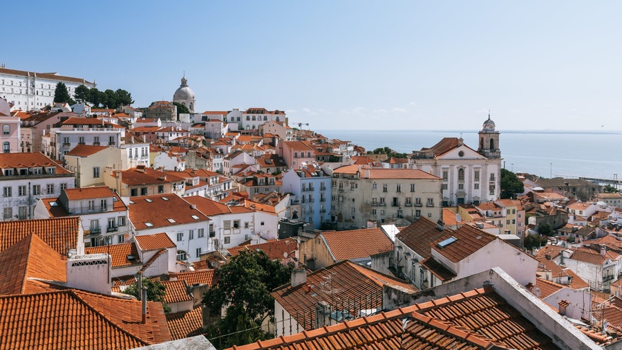 A coastal town with terracotta-roofed buildings, a prominent church with a dome, and a sea view.