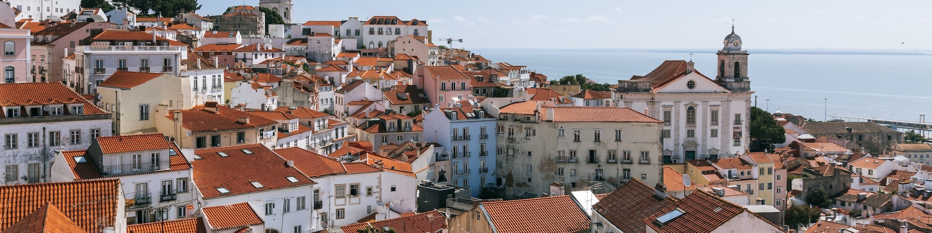 A coastal town with terracotta-roofed buildings, a prominent church with a dome, and a sea view.