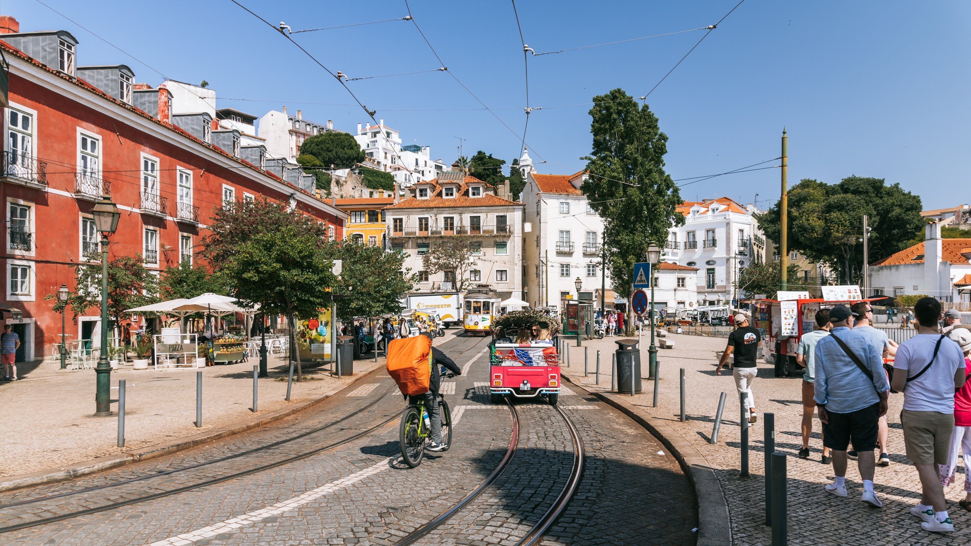 A tram on a cobblestone street with buildings and a hill in the background.
