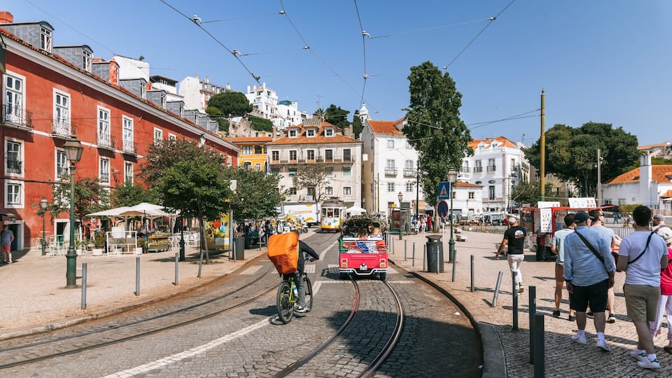A tram on a cobblestone street with buildings and a hill in the background.