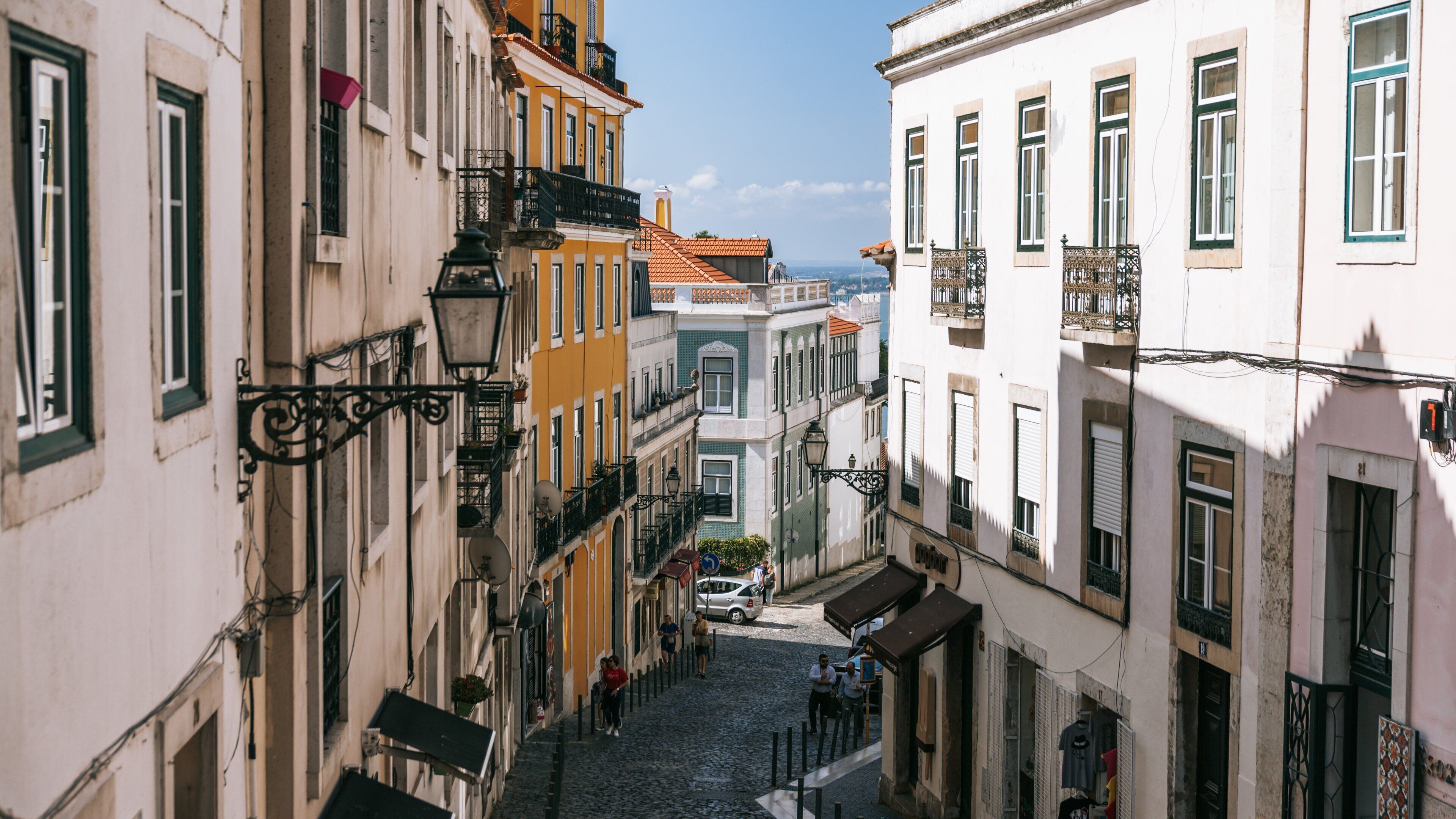 A narrow cobblestone street flanked by colorful buildings with balconies and traditional European architecture.