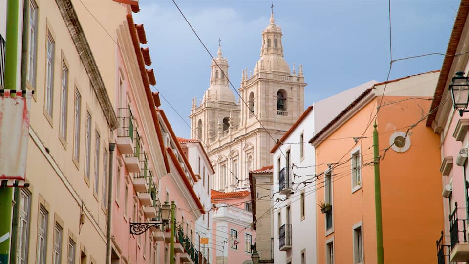 A narrow street with colorful buildings and a prominent church with two towers.
