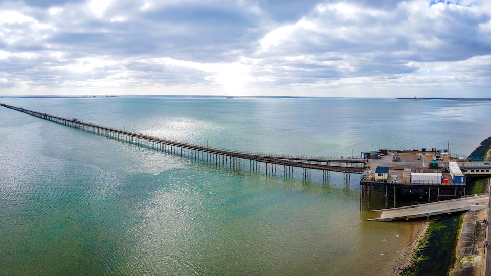 A pier extending into a calm body of water, a coastal amusement park, and distant buildings.