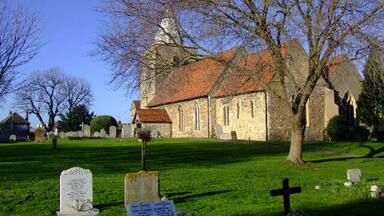 A church with a red-tiled roof, a graveyard with headstones, and leafless trees.