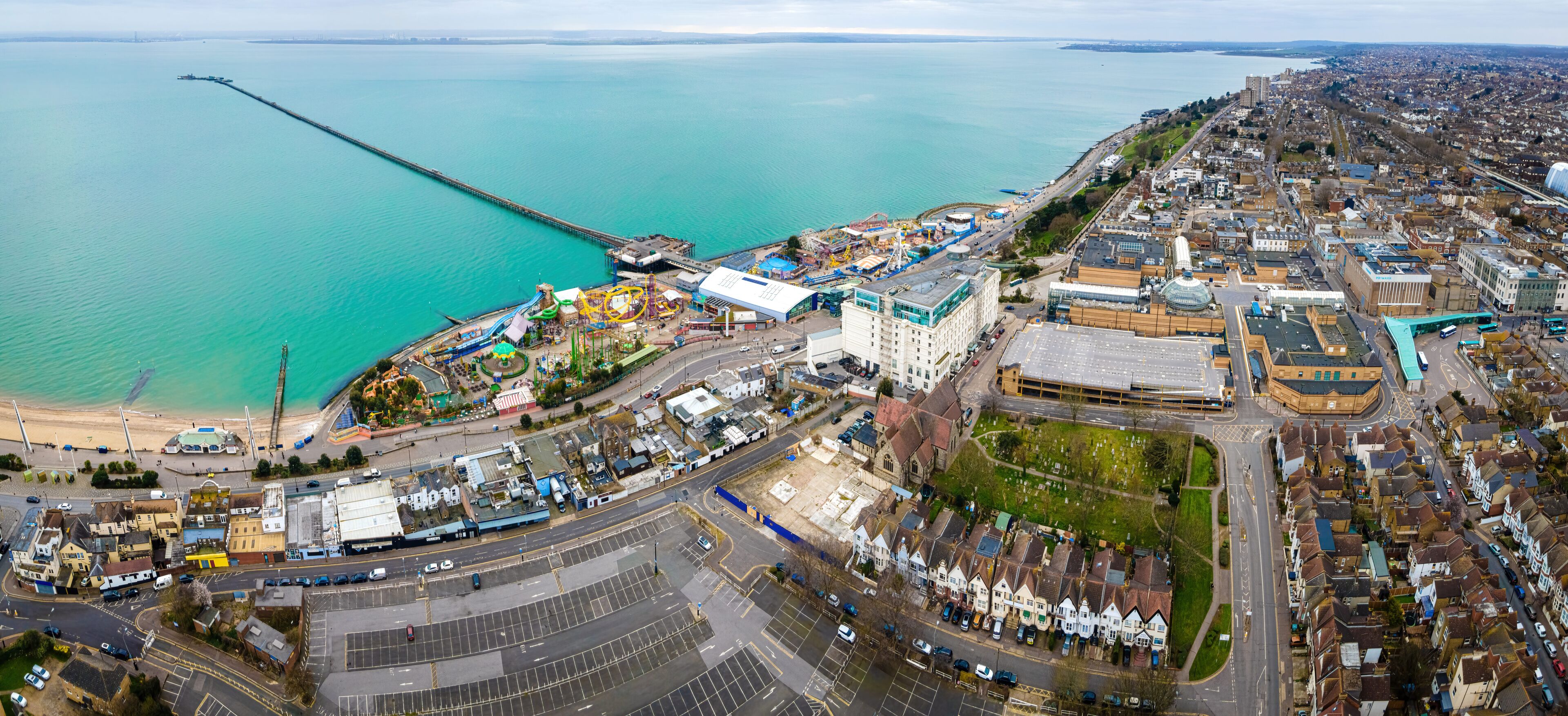 An aerial view of a coastal city with a pier extending into the sea, a waterfront amusement park, and residential areas with houses.
