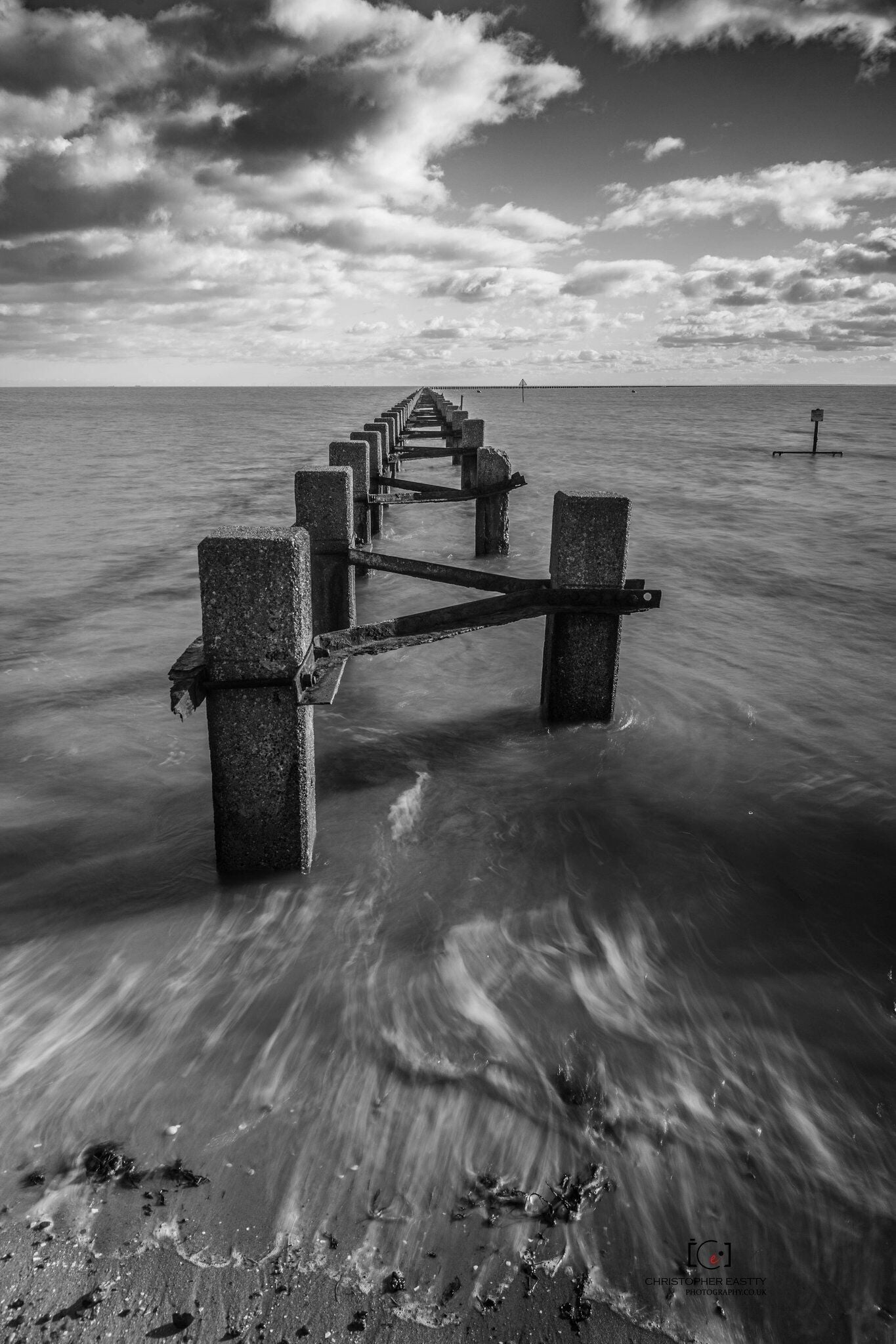A pier extending into calm waters with a cloudy sky above.