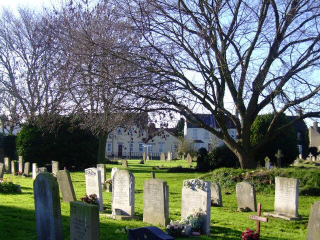A cemetery with headstones and a large tree in the foreground.