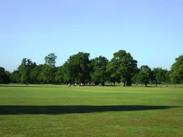 Open-air exercise class, Tooting Bec Common A group of about 15/20 women in an open-air class, standing in a circle playing 'tag', next to Doctor Johnson Avenue.