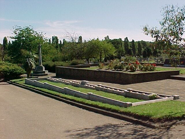 War memorial and children's mass grave, Hither Green Cemetery, S.E. London. Hither Green Cemetery covers 65 acres. Almost in the centre is a memorial to all the people of Lewisham who died in the Second World War. In the foreground is a grave containing 31 children aged 5-15, and a teacher. The local Sandhurst Road School was bombed in 1943. 38 children and 6 adults died. Behind the trees in the background is the railway line into London. About 1/2 a mile from this spot lived E. Nesbit who wrote The Railway Children.