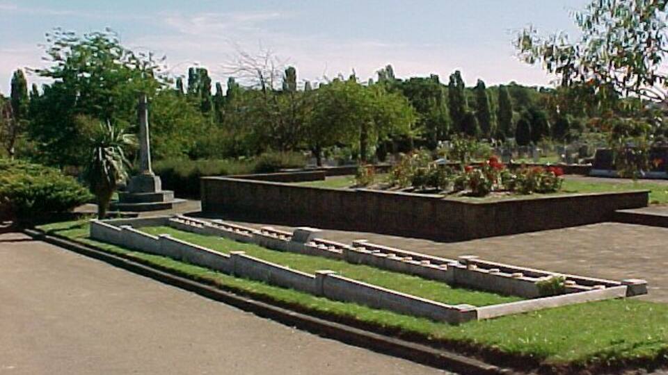 War memorial and children's mass grave, Hither Green Cemetery, S.E. London. Hither Green Cemetery covers 65 acres. Almost in the centre is a memorial to all the people of Lewisham who died in the Second World War. In the foreground is a grave containing 31 children aged 5-15, and a teacher. The local Sandhurst Road School was bombed in 1943. 38 children and 6 adults died. Behind the trees in the background is the railway line into London. About 1/2 a mile from this spot lived E. Nesbit who wrote The Railway Children.