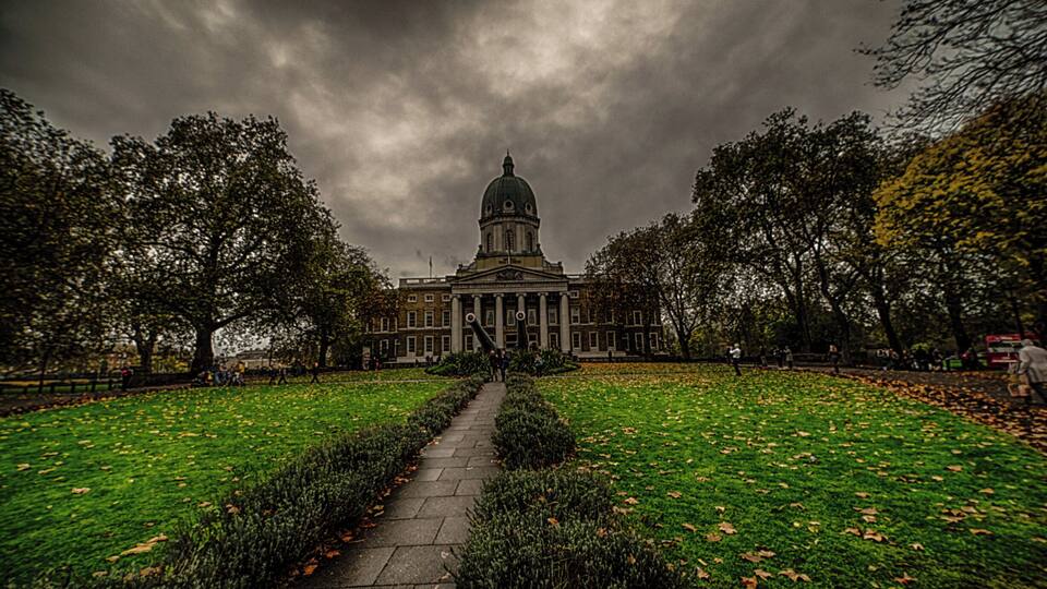 A grand building with a dome, surrounded by a well-maintained lawn and a pathway leading to it.