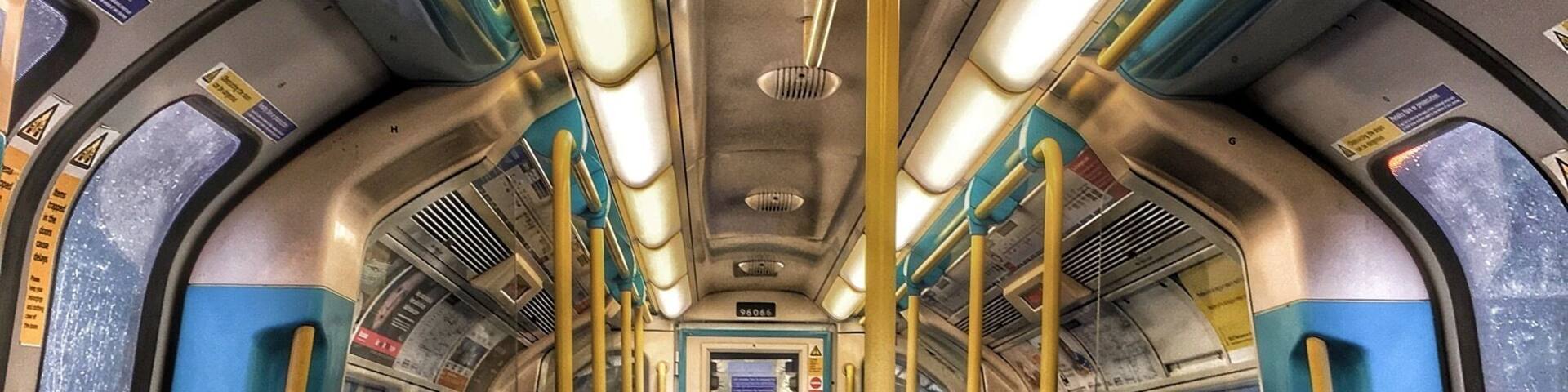 An empty subway car with blue seats and yellow poles.