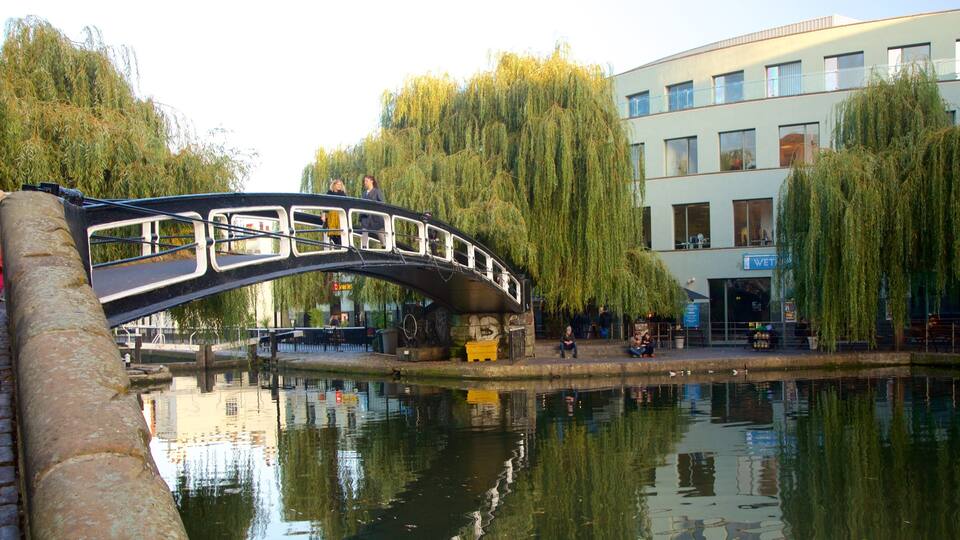 A stone bridge over a calm river, surrounded by willow trees and a modern building.