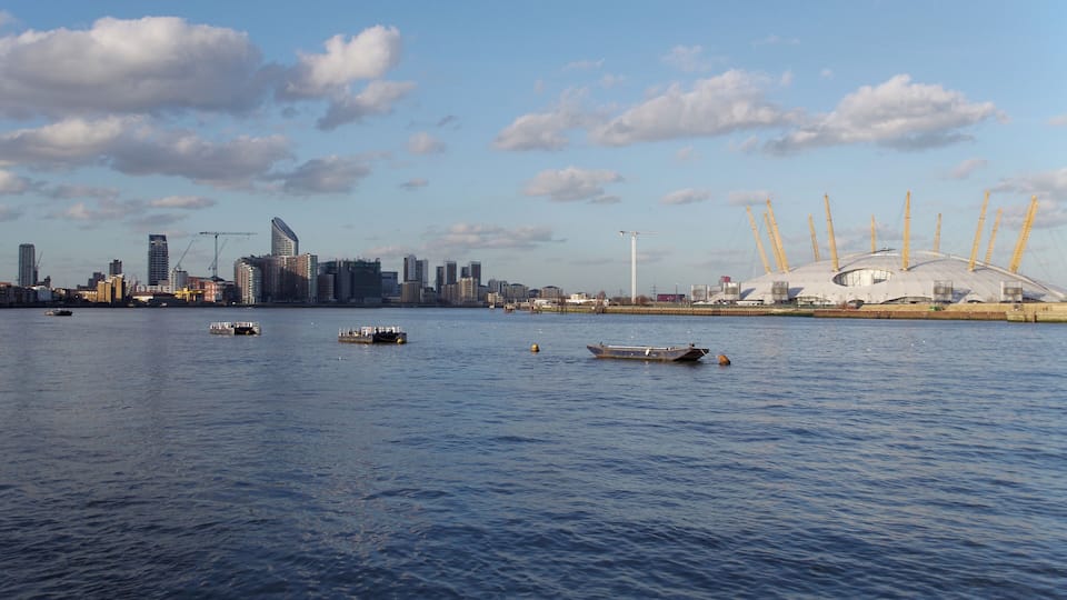 A river with boats, a city skyline, and a large stadium with cranes.