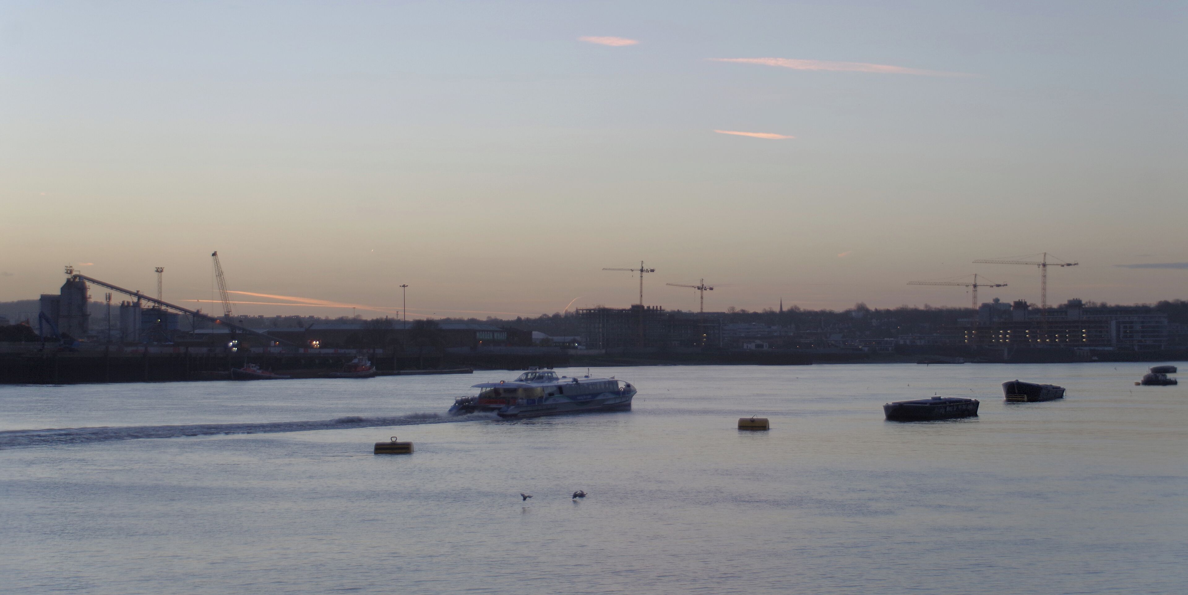 A Thames Clipper speeds west along the Thames, past Greenwich, just before sunrise. This was taken from near the eastern end of the City Canal.