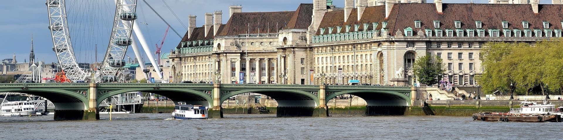 A large Ferris wheel, a bridge, and historic buildings by a river.