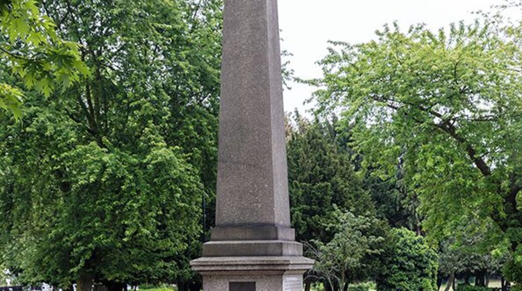 The "monument' in the image is a memorial drinking fountain. Erected in 1879, it originally stood in the middle of the road a little further to the south at the junction with Park Avenue. It was moved in 1904 to accommodate new tram routes. The main inscription on east face reads 'Erected in affectionate remembrance of Mrs Catherine Smithies of Earlham Grove, Wood Green, Founder of the Band of Mercy Movement, and presented by her family and friends for the use of the public'. The stone forming the obelisk is twenty-one feet in length. In 1879 it was the longest single cut stone in London, with the exception Cleopatra's Needle on the Thames Embankment. Made of polished granite, it was quarried from the Penryn quarries of Freeman and Sons, in Cornwall.
