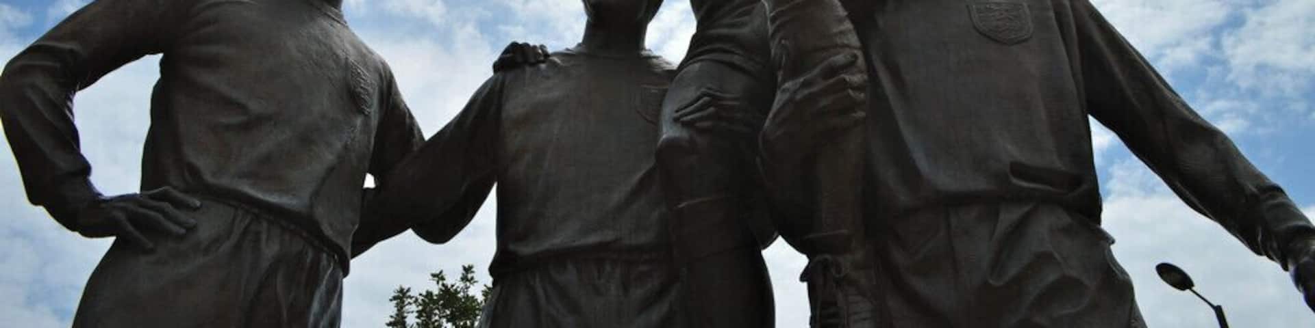 A group of statues with one figure raising a fist against a cloudy sky.