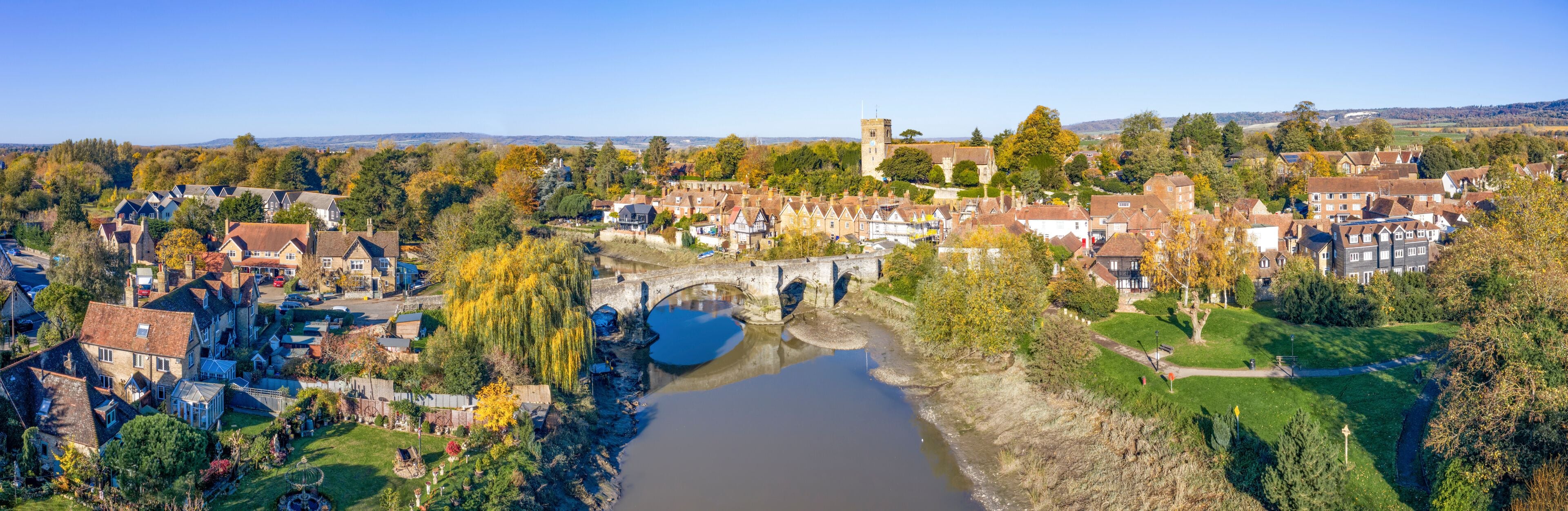 Un pueblo histórico con un río, un puente y una torre de iglesia.