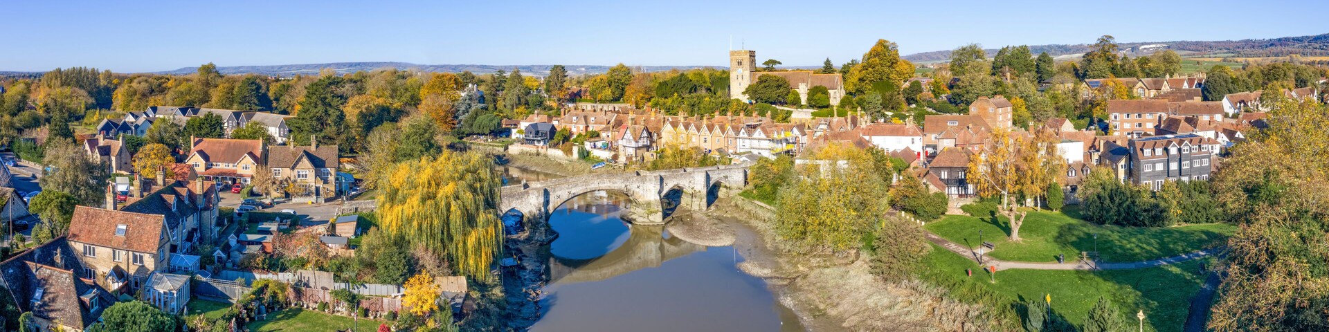 Un pueblo histórico con un río, un puente y una torre de iglesia.