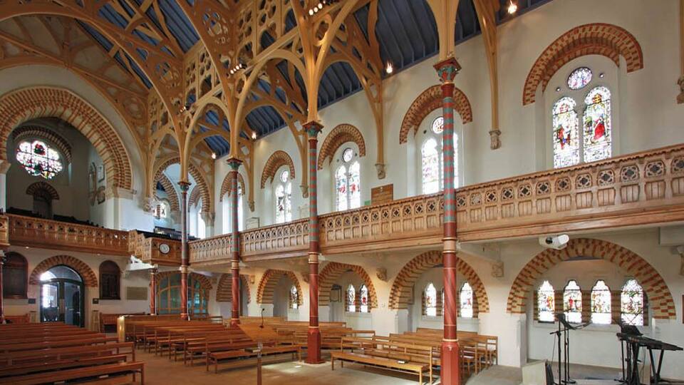 A church interior with arched ceilings, stained glass windows, wooden pews, and a balcony.