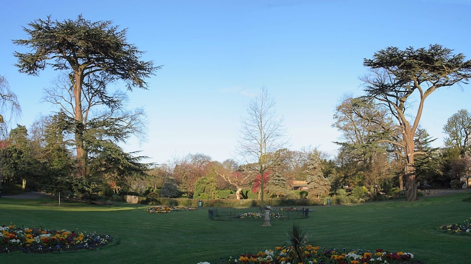 Ein Park mit großen Bäumen, Blumenbeeten und einem gepflegten Rasen.