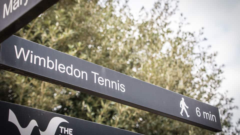 Directional signs with 'Wimbledon Tennis' and a walking symbol indicating a 6-minute walk.