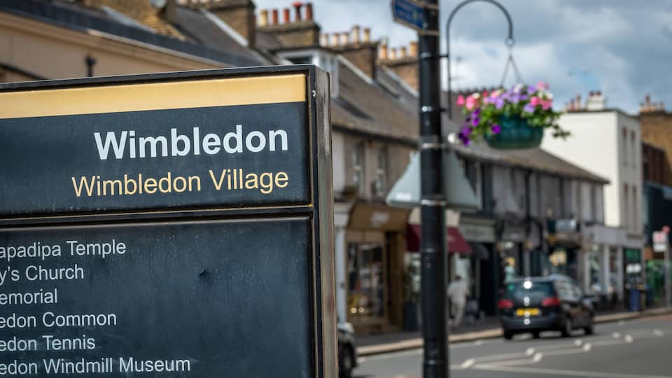 A sign listing attractions in Wimbledon Village, including the Wimbledon Tennis Centre and the Windmill Museum.