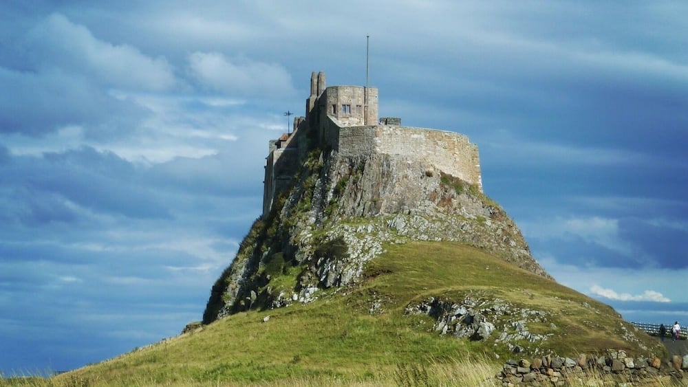 A castle on a grassy hill under a cloudy sky.