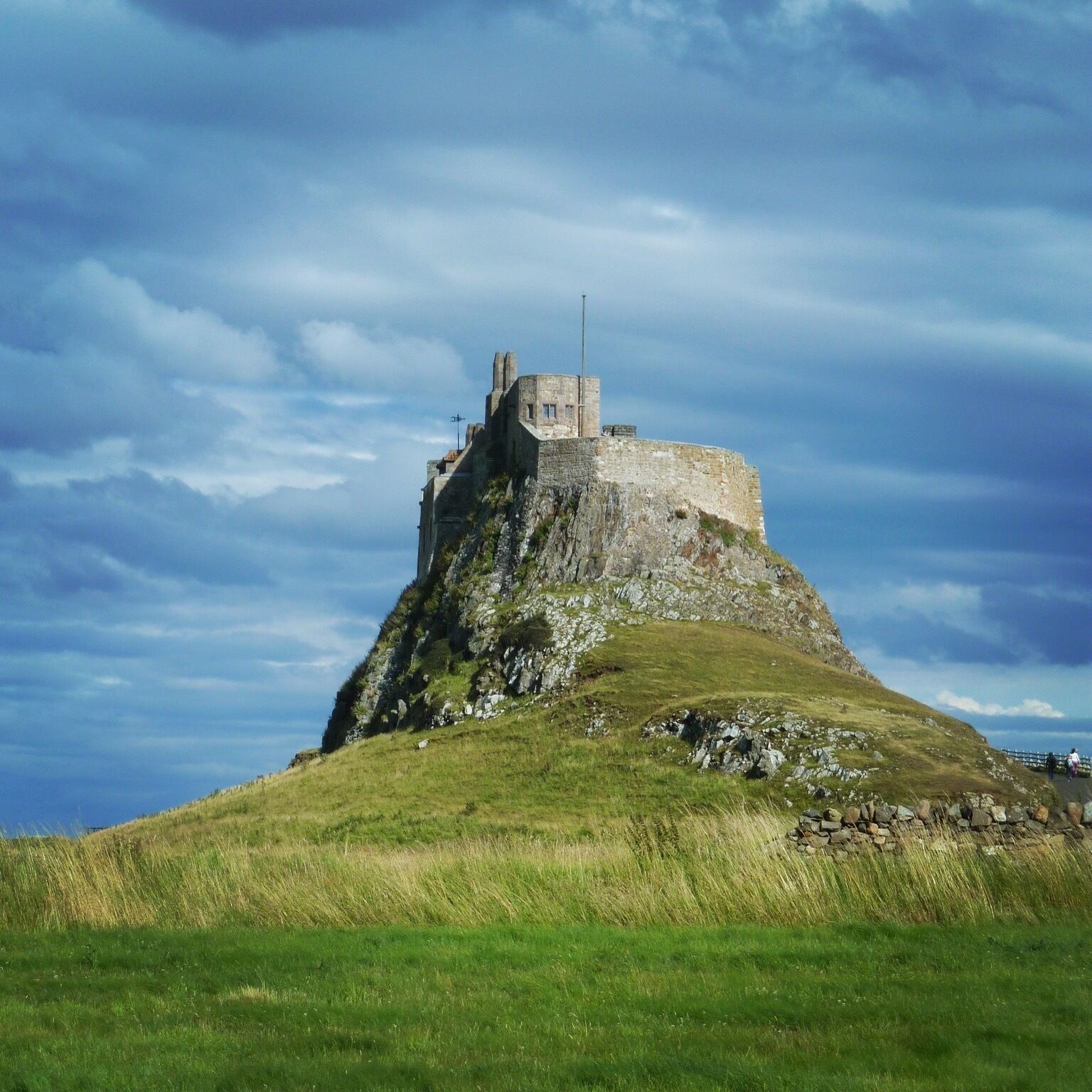 A castle on a grassy hill under a cloudy sky.