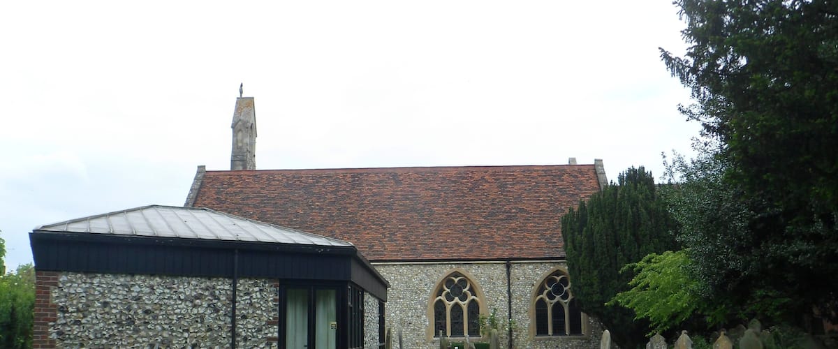 A stone church with a tiled roof, a wooden bench, and a grassy area with white flowers.