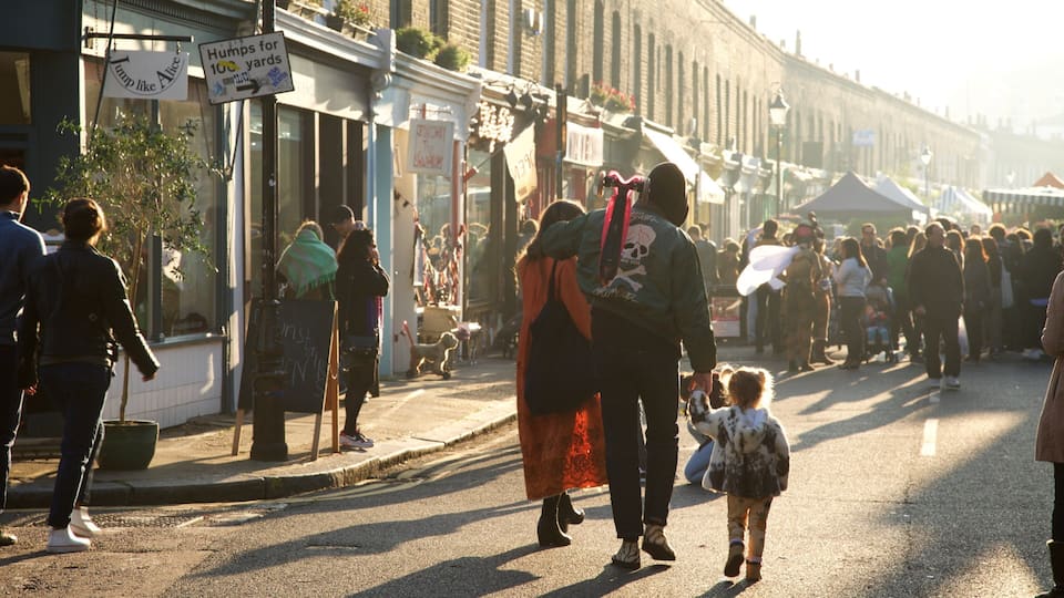 A busy street with people walking, a sign that reads "Humps for 100 yards", and a crowd gathered near a tent.