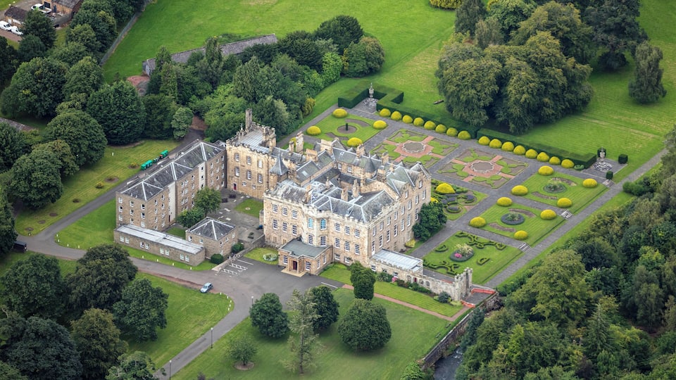 An aerial view of a historic castle surrounded by lush gardens and trees.