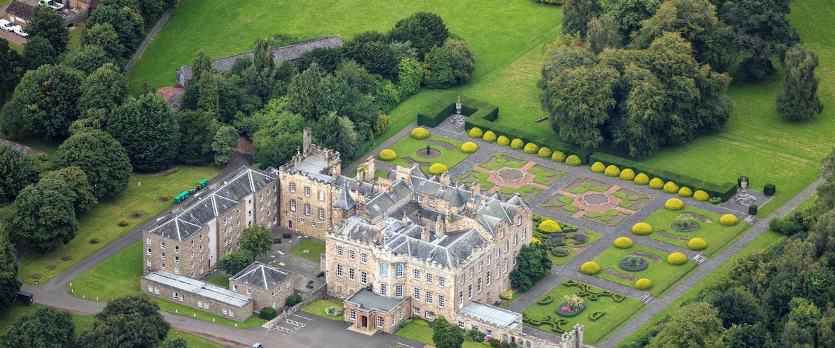 An aerial view of a historic castle surrounded by lush gardens and trees.