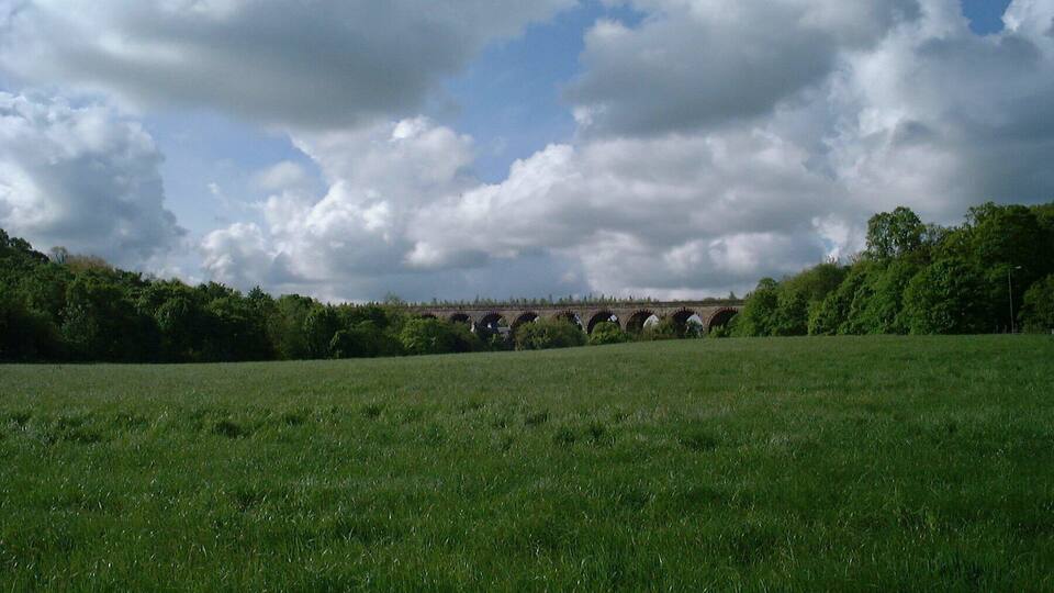 A green field, a stone bridge, and a cloudy sky.
