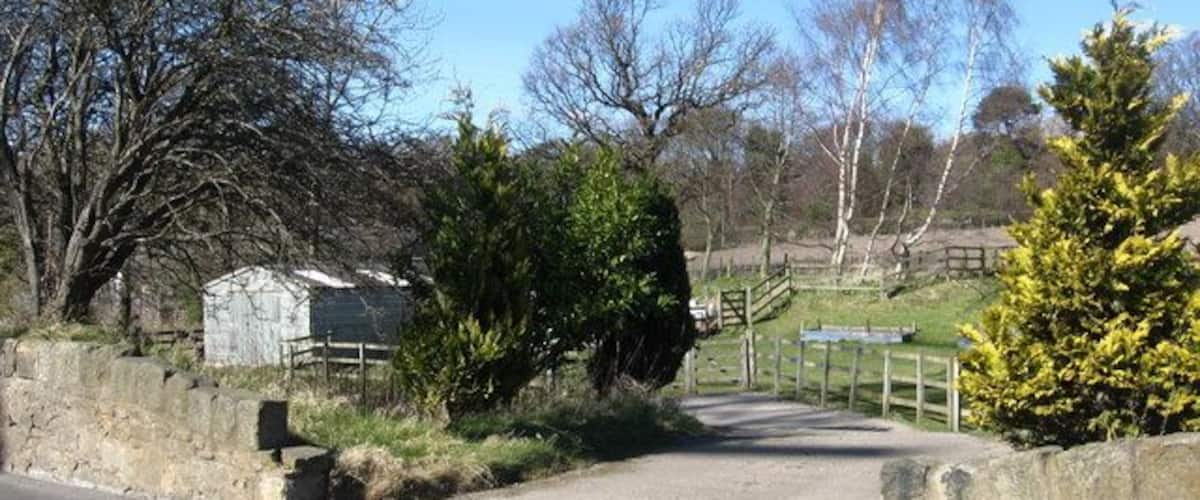 A rural road leading to a stone bridge over a small stream, surrounded by trees and a stone wall.