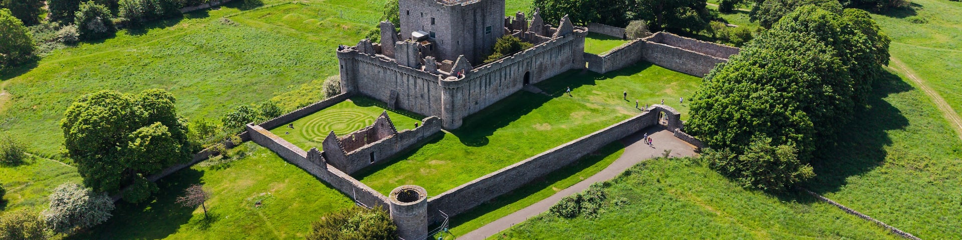 A medieval castle surrounded by lush green fields and trees.