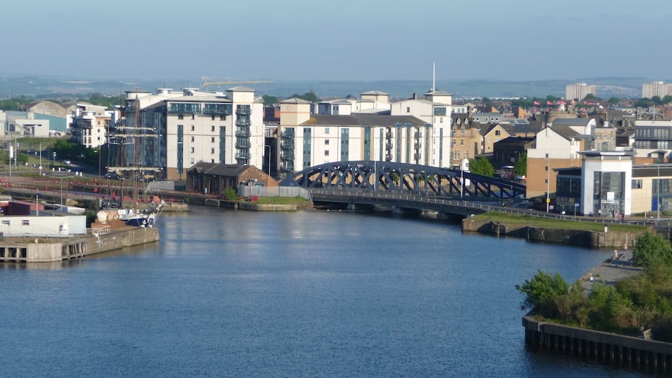 A river with a bridge, buildings, and a distant view of a cityscape.