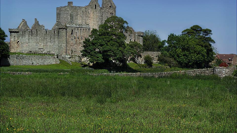 Eine historische Burg, umgeben von üppigen grünen Feldern und Bäumen.