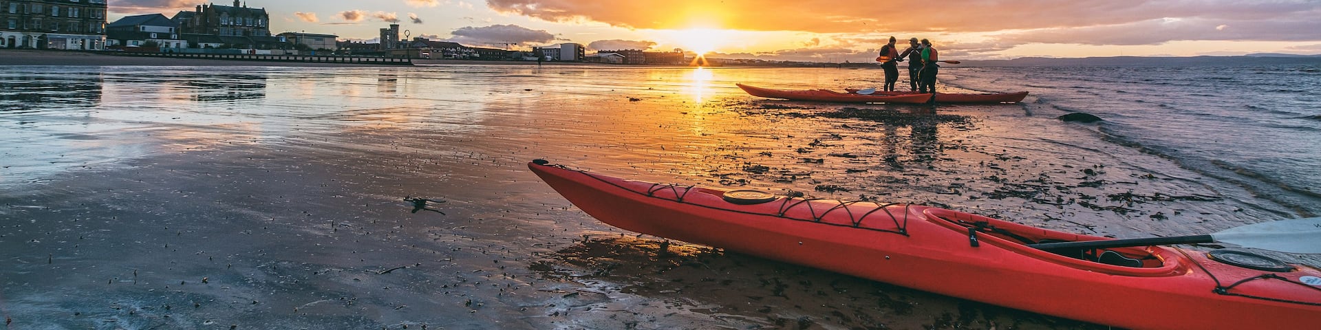 A sunset over a beach with kayaks and people.