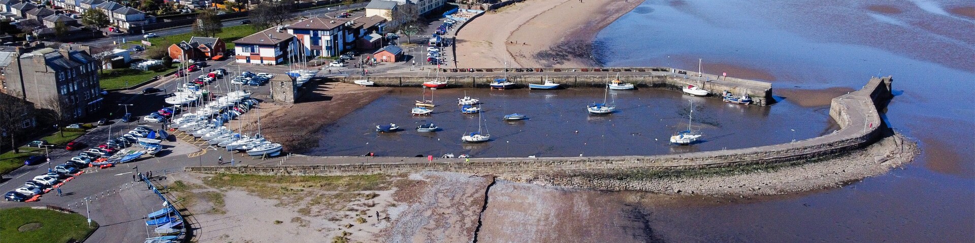 Uma vila costeira com um porto de recreio, praia de areia e edifícios residenciais.