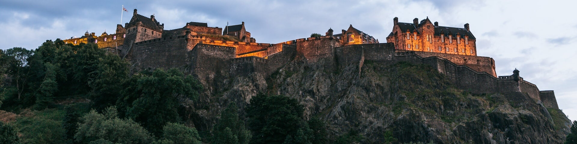 A historic castle on a rocky hill with surrounding greenery.