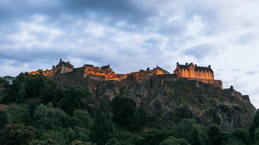A historic castle on a rocky hill with surrounding greenery.