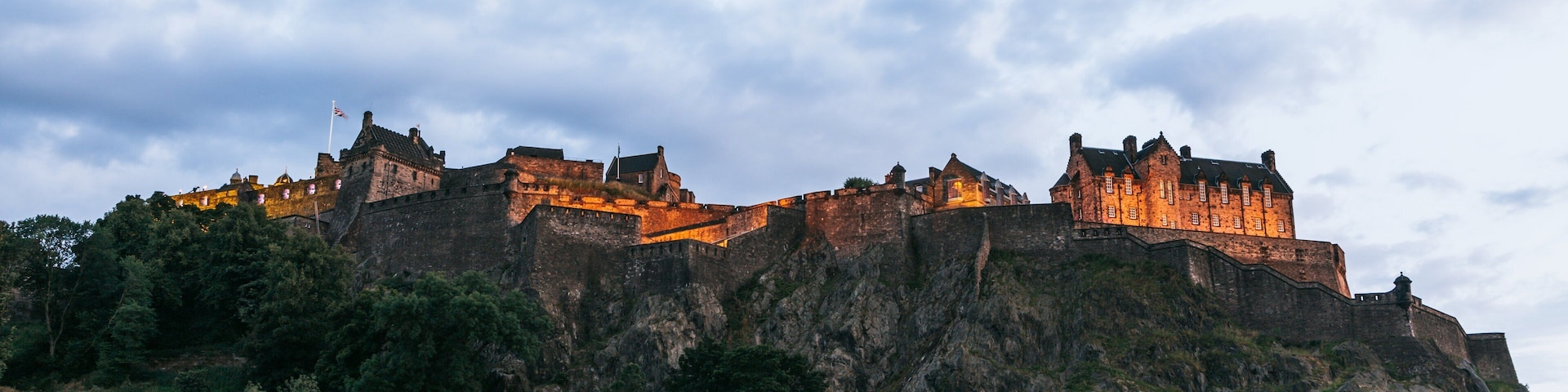 Um castelo histórico numa colina rochosa, rodeado por vegetação.