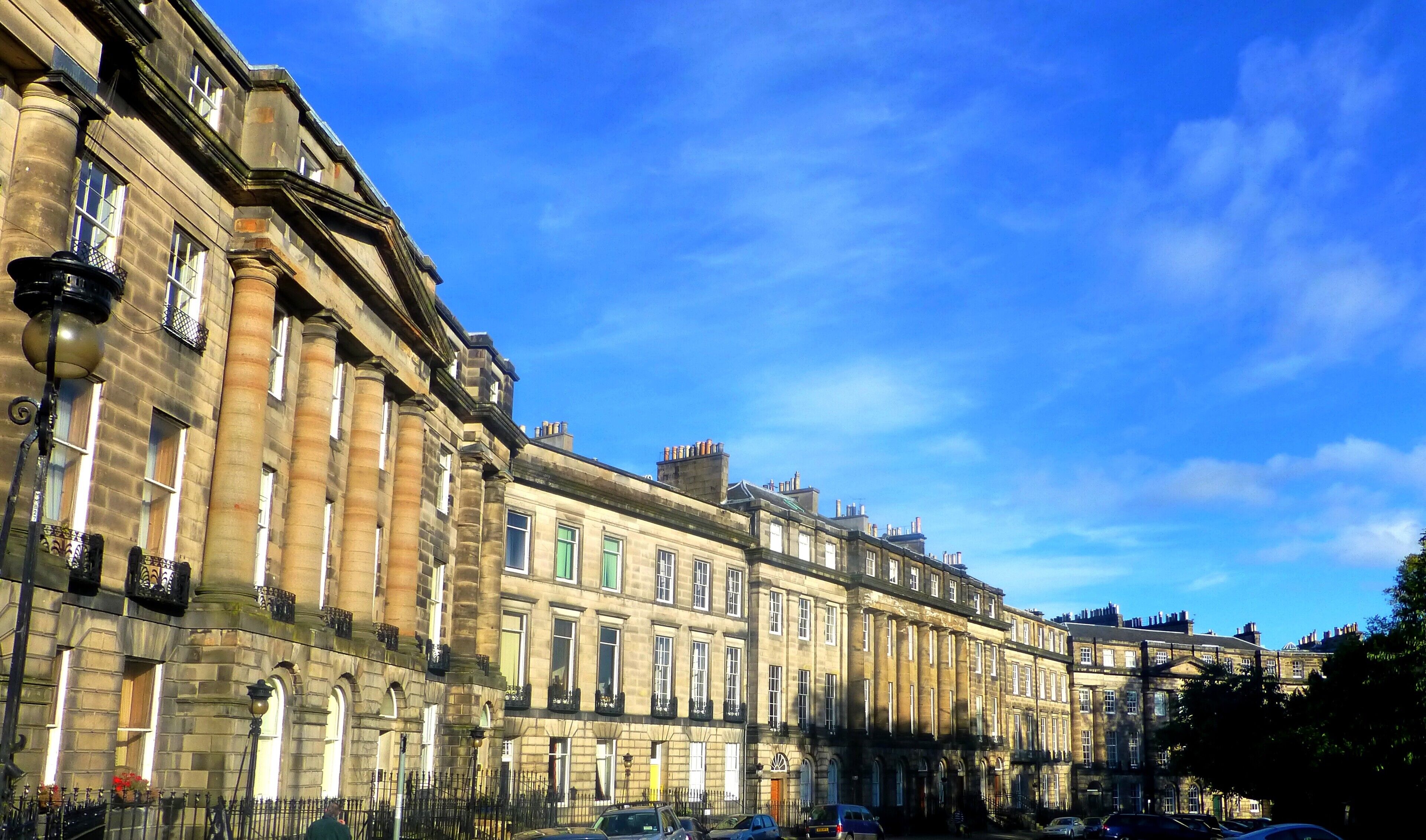 A row of historic stone buildings with large windows and ornate balconies under a clear blue sky.
