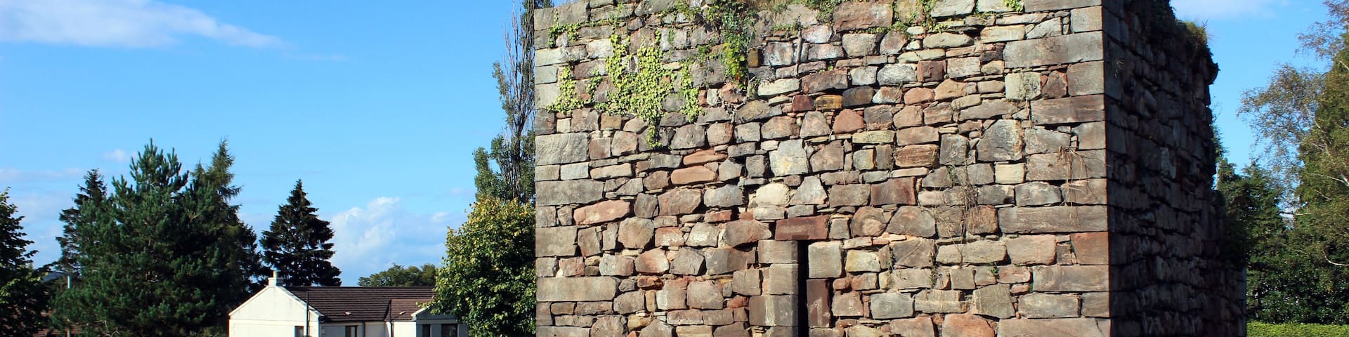 A stone structure with a window, surrounded by a grassy field and trees.