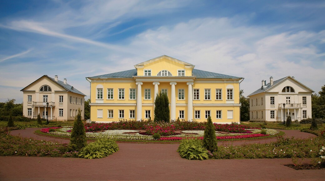 Ein großes, gelbes Gebäude mit einer symmetrischen Fassade, umgeben von einem gepflegten Garten mit verschiedenen Blumen und Sträuchern.